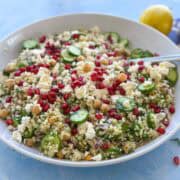 Close-up of a healthy Mediterranean bulgur salad with chickpeas, feta, herbs, and cucumber slices on a light blue background.