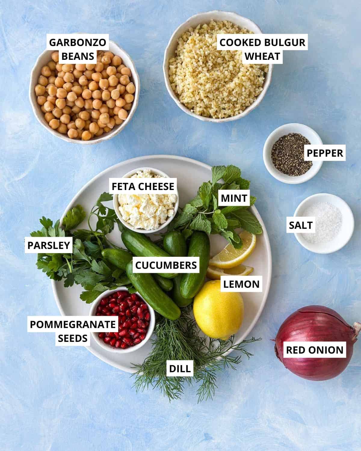 Top view of Mediterranean bulgur salad ingredients, including cooked bulgur, chickpeas, cucumbers, feta, red onion, herbs, lemon, and pomegranate seeds.