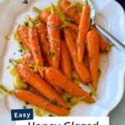 Plate of glossy, oven-roasted honey glazed carrots topped with herbs and served with a spoon. A sweet and savory vegetable side dish for fall, Easter, or everyday dinners.
