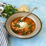 Close-up of Italian Bean Soup in a rustic bowl with beans, kale, carrots, and cherry tomatoes in a rich tomato broth, garnished with Parmesan.