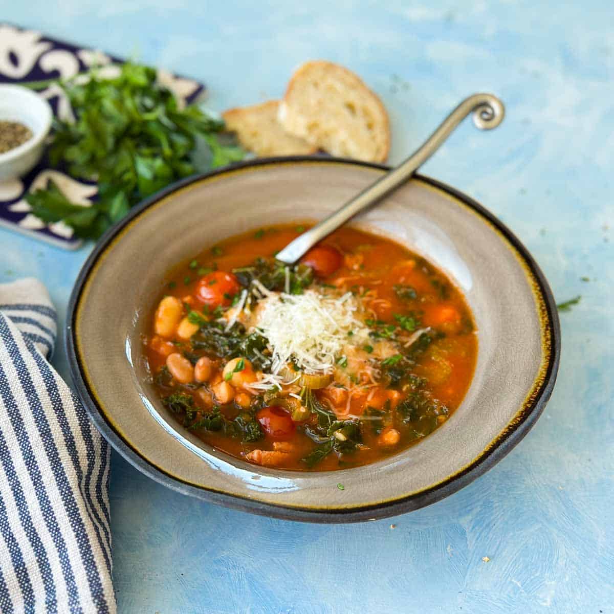 Close-up of Italian Bean Soup in a rustic bowl with beans, kale, carrots, and cherry tomatoes in a rich tomato broth, garnished with Parmesan.