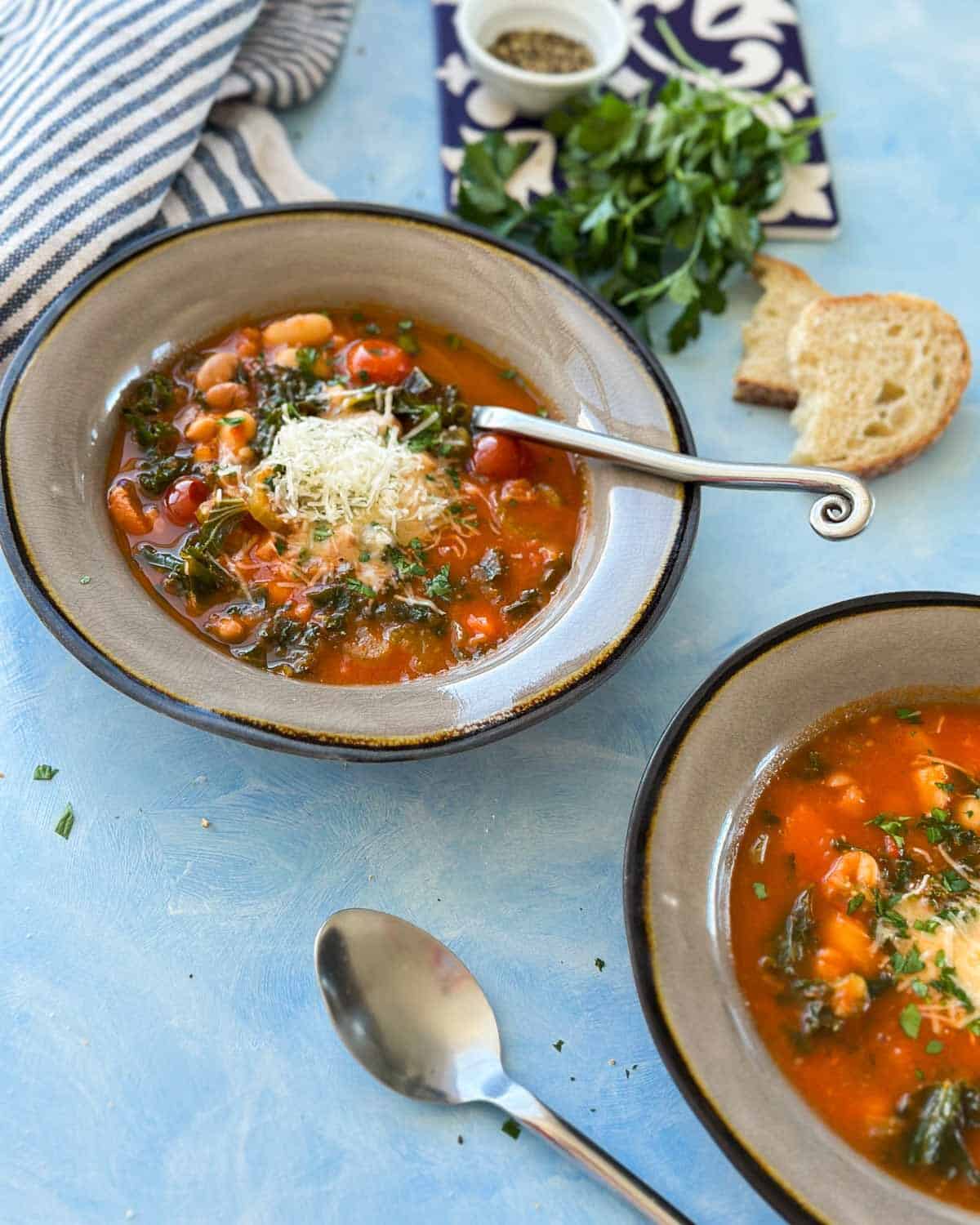 Side view of Italian Bean Soup in a rustic bowl, filled with beans, kale, carrots, and tomatoes, topped with Parmesan cheese and parsley.