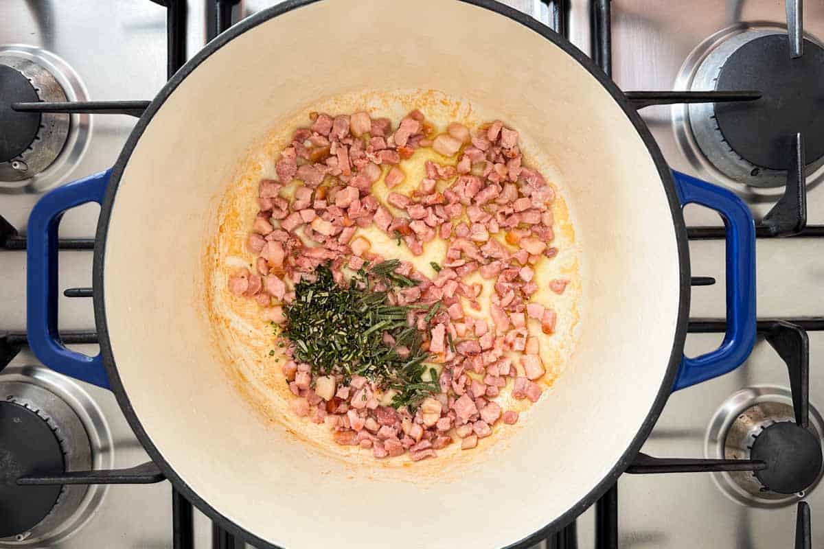 Chopped rosemary and sage added to sizzling bacon in a Dutch oven while preparing Italian Bean Soup.