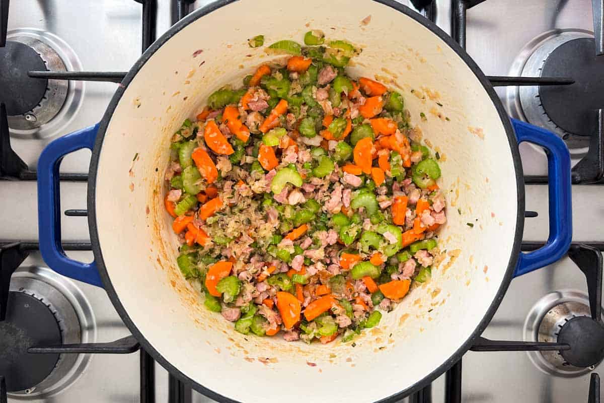 Carrots and celery cooking with bacon, onion, and herbs in a Dutch oven to build the base of Italian Bean Soup.