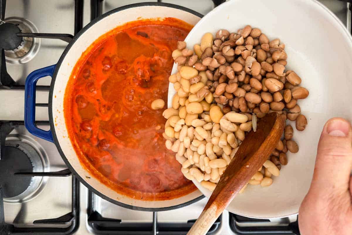 Canned mixed beans being added to the tomato broth while cooking Italian Bean Soup.