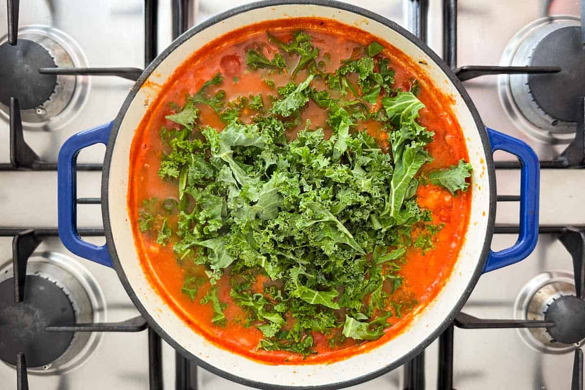 Fresh kale added into the simmering tomato and bean broth for Italian Bean Soup.