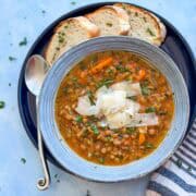 Cozy bowl of Veggie Lentil soup served with crusty bread slices, garnished with shaved Parmesan and herbs.