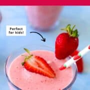 Glass of creamy strawberry banana smoothie topped with a halved fresh strawberry and garnished with a whole strawberry and a cute strawberry-print straw.