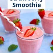 Three glasses of bright pink strawberry banana smoothie served with halved strawberries and fun straws, styled on a light blue background.
