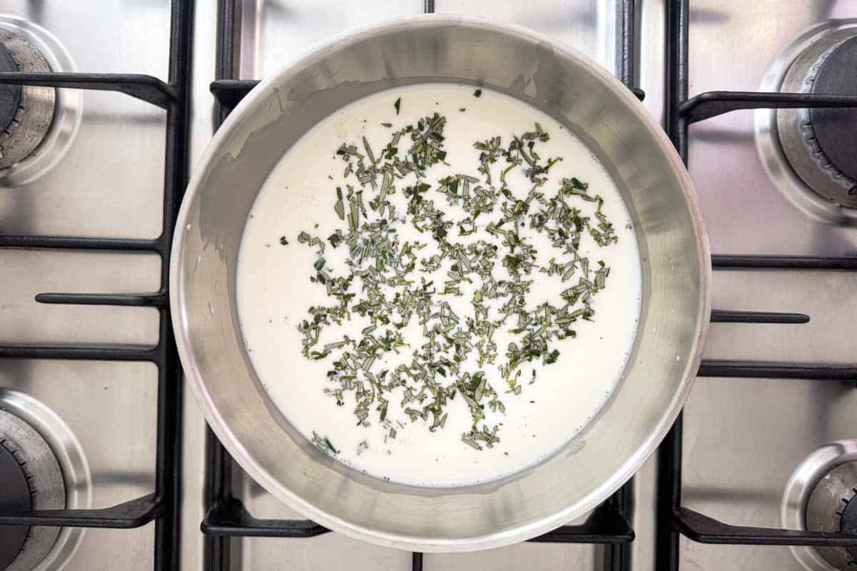 Whole milk and chopped rosemary warming in a saucepan to start creamy parmesan polenta.
