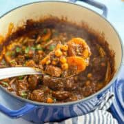 Spoonful of Moroccan lamb tagine with apricots and chickpeas held above the pot. Steam rising highlights this authentic Moroccan lamb dish.