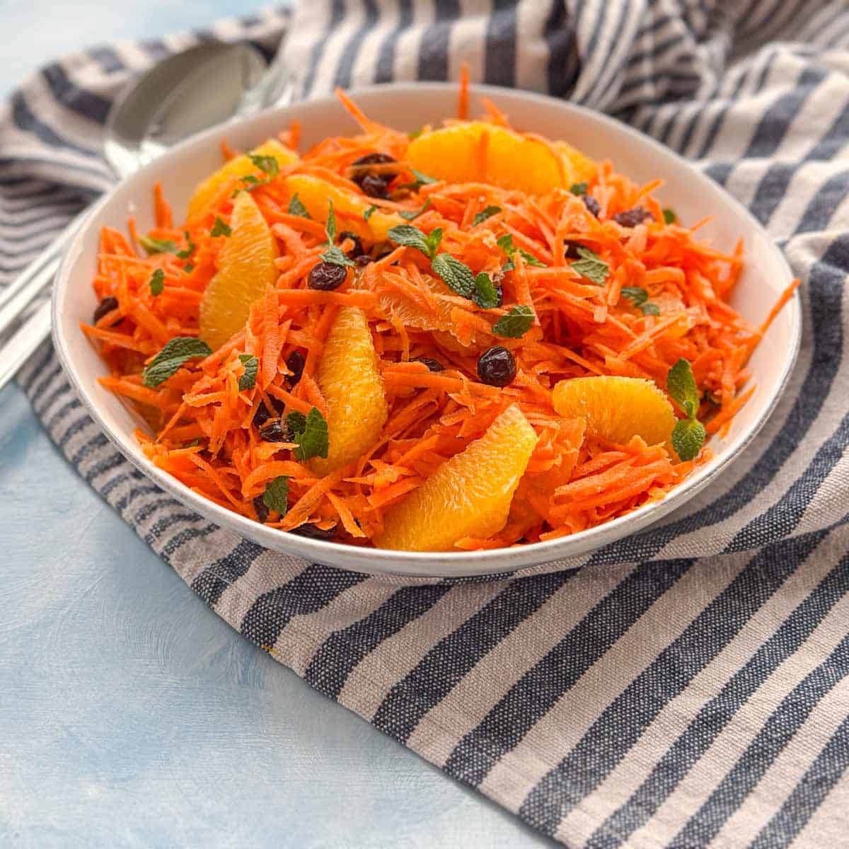 Refreshing carrot mint salad with oranges and raisins, a Moroccan-inspired side dish served in a white bowl.