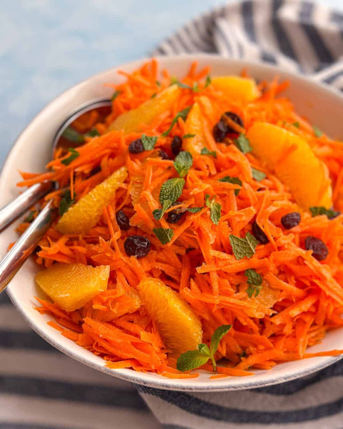 Close-up side angle of Moroccan carrot raisin salad with grated carrots, orange slices, and mint leaves.