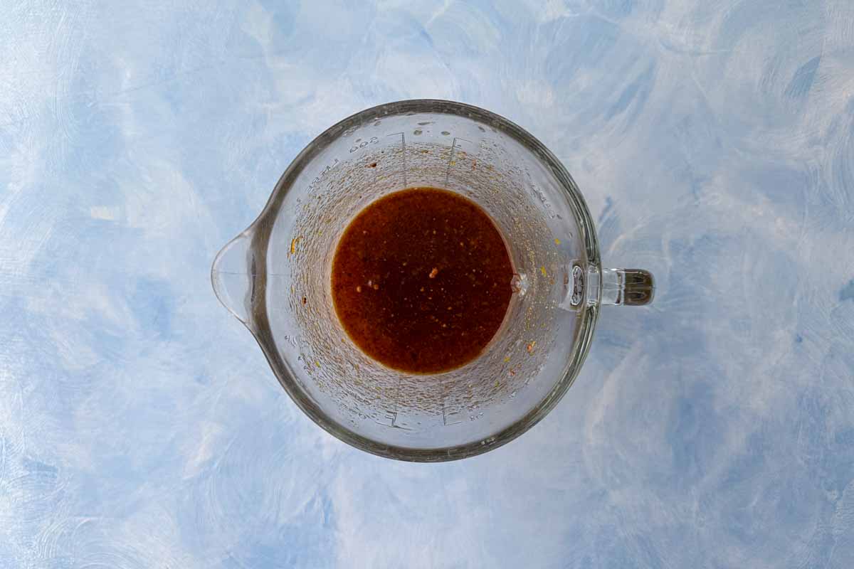 Homemade Moroccan carrot salad dressing in a glass jug, made with olive oil, apple cider vinegar, honey, and spices.