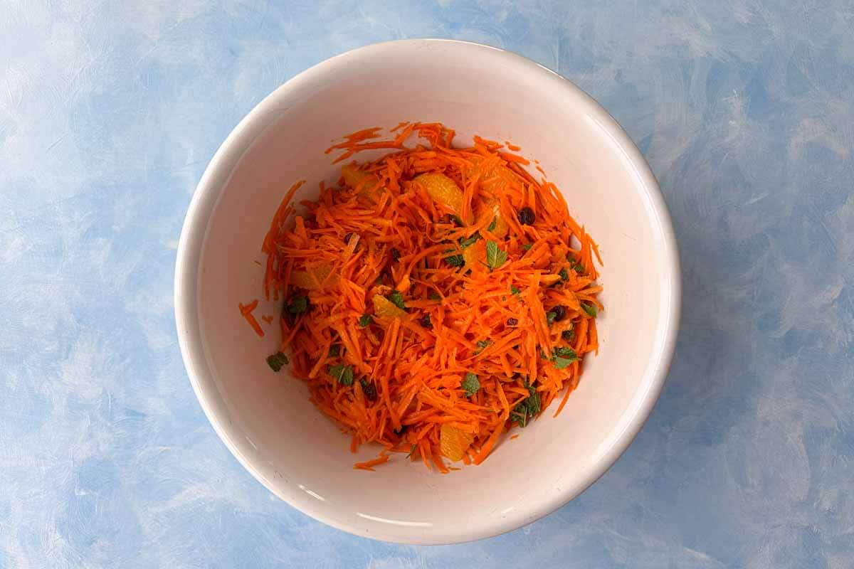 Finished Moroccan carrot salad in a white bowl, tossed with oranges, raisins, fresh mint, and spiced dressing