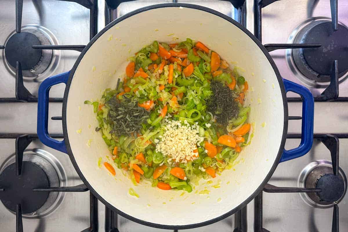 Sautéed vegetables with minced garlic, thyme, and sage added to a Dutch oven for building flavor in chicken orzo soup.