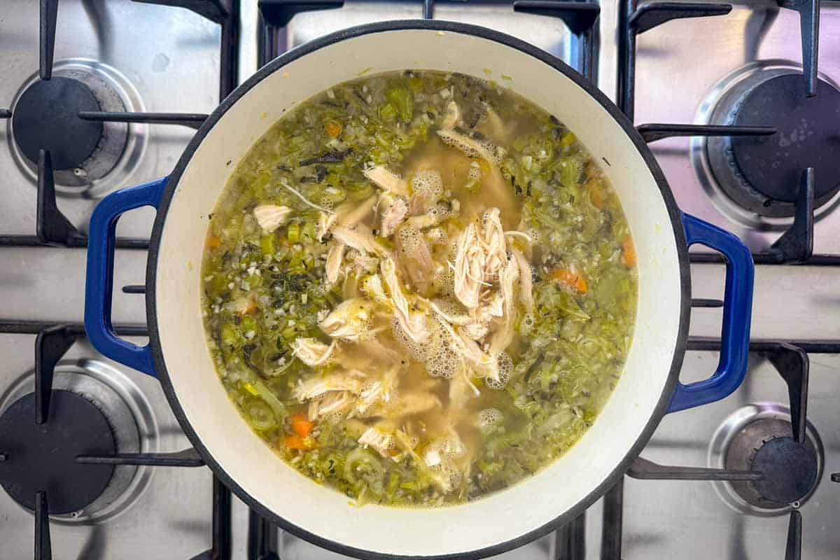 Shredded rotisserie chicken simmering with vegetables and broth in a pot, the base of homemade chicken orzo soup.