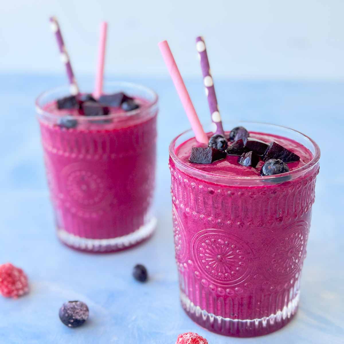 Close-up of a rich pink beetroot smoothie in a textured glass, topped with blueberries and small beetroot pieces.