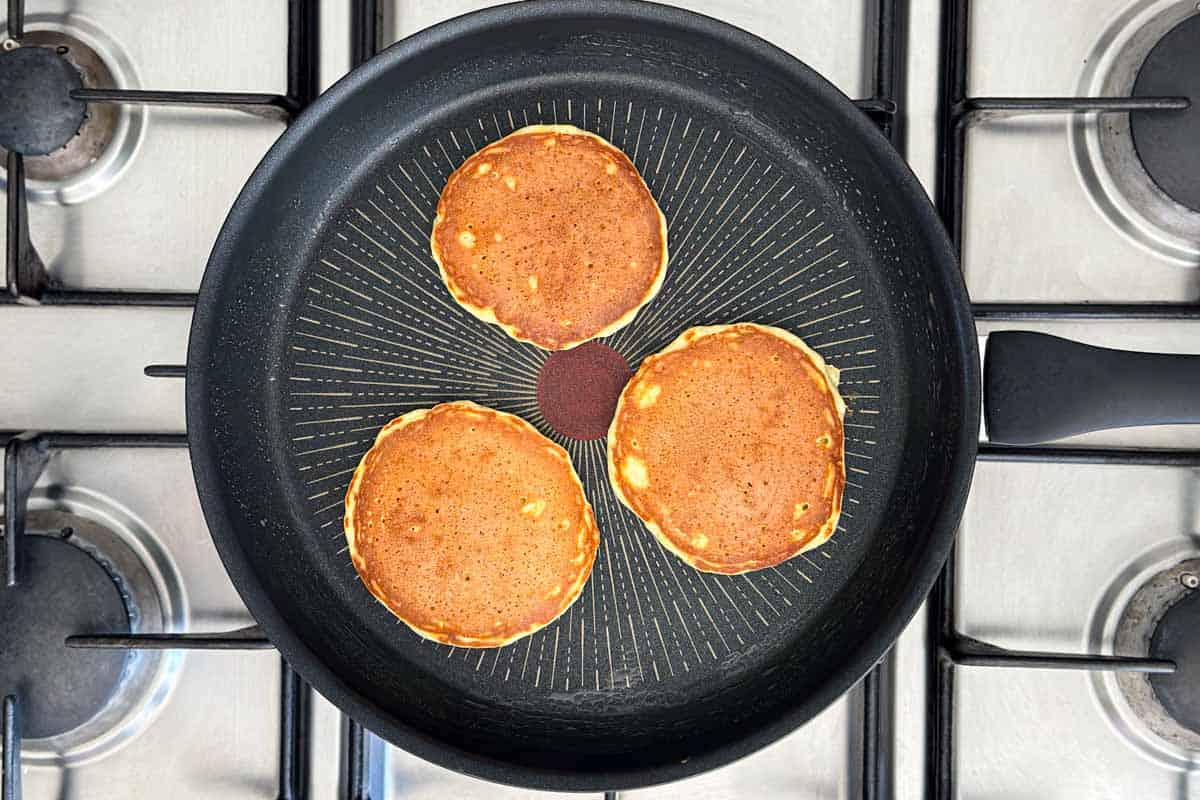 Golden brown pancakes cooking evenly in a pan after flipping, showing a perfectly caramelized surface.