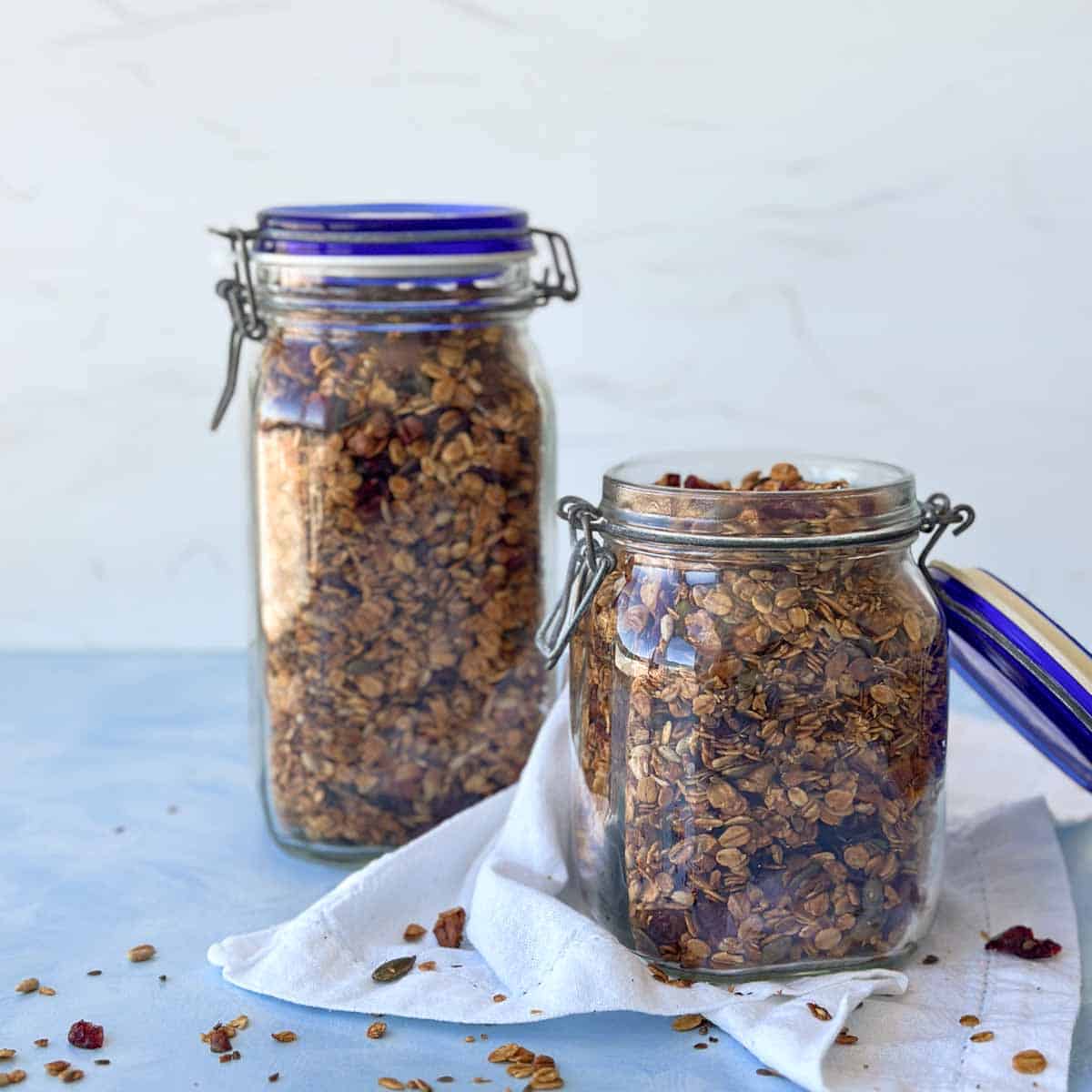 Two jars filled with golden baked homemade granola placed on a soft cloth, highlighting texture and natural ingredients.