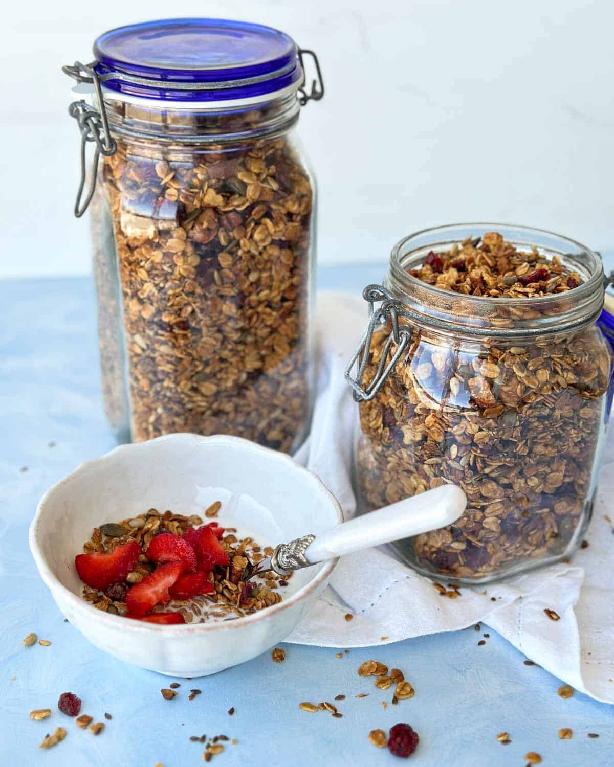 Tilted glass jar spilling homemade granola onto a cloth, showcasing crunchy clusters and wholesome ingredients.