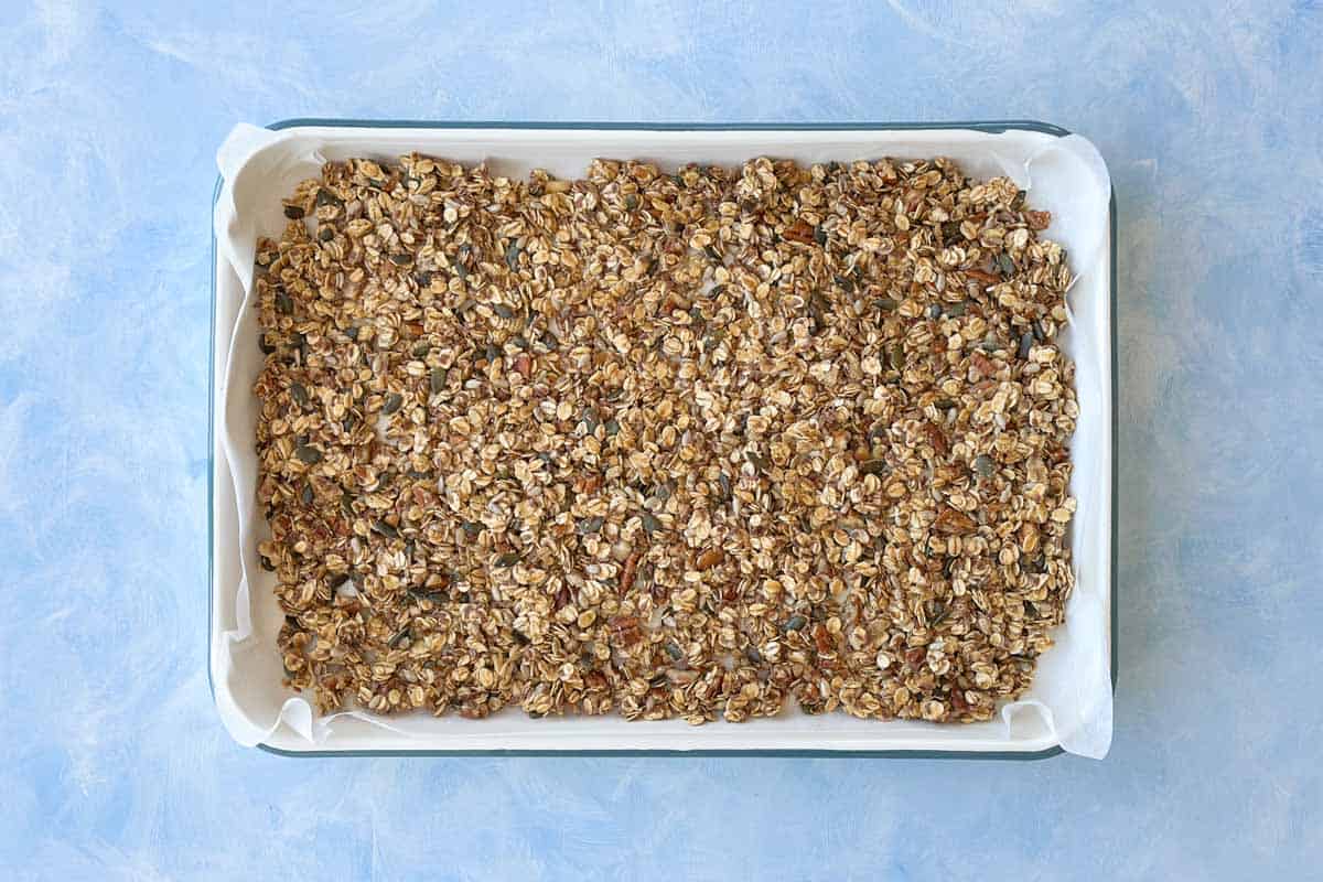 Unbaked granola spread evenly on a lined baking tray, ready to be baked until golden and crisp.