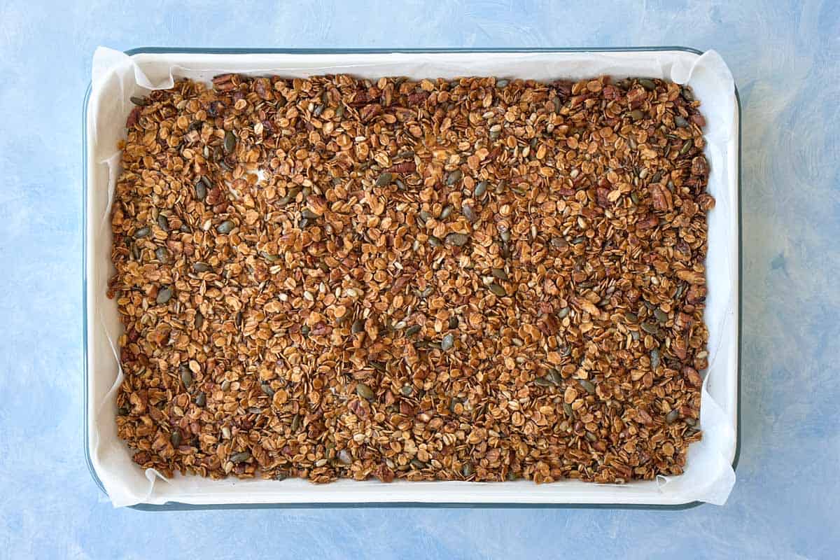 Freshly baked granola on a tray with a golden brown color, showing crunchy clusters forming during baking.