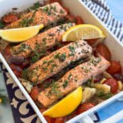 Close-up of Mediterranean baked salmon topped with fresh herbs and lemon, surrounded by juicy roasted tomatoes.