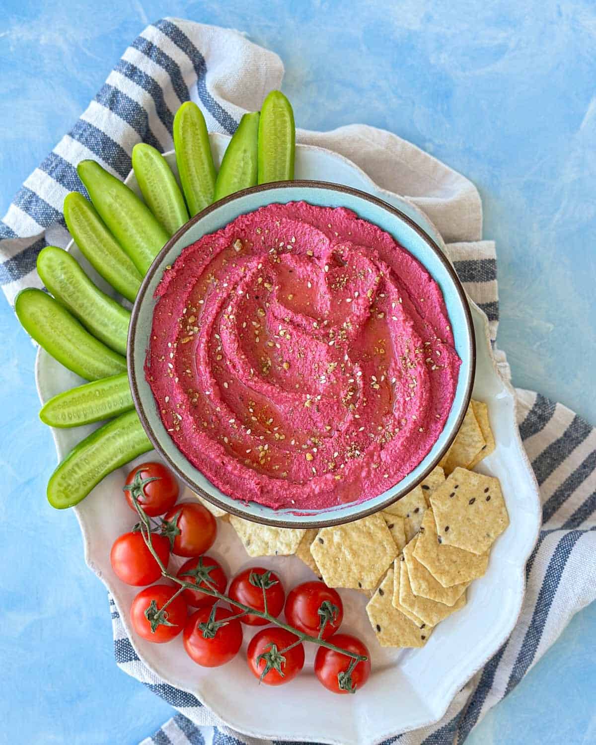 Overhead shot of beetroot hummus with olive oil and spices, presented on a serving plate with fresh vegetables and crackers.