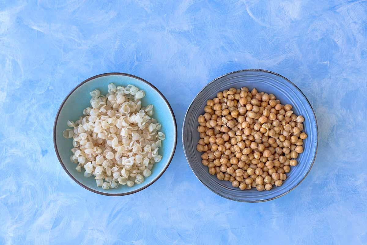 Cooked Garbanzo beans deshelled in one bowl and the discarded casings in another bowl.