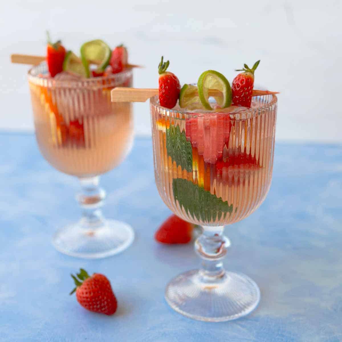 Strawberry rosé sangria recipe served over ice in ribbed goblet glasses, garnished with fresh strawberries, lime slices, orange slices, and mint leaves.
