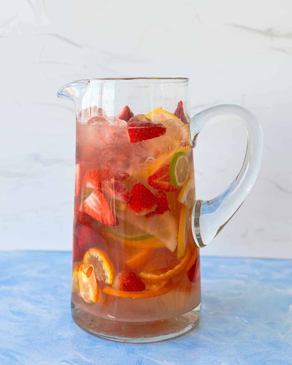 Chilled rosé sangria in a glass pitcher, filled with strawberries and bright citrus slices, ready to serve for a relaxed summer gathering.
