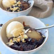 Bowl of self-saucing chocolate pudding served with a poached pear, vanilla ice cream, and scattered almonds, showing the molten chocolate sauce.