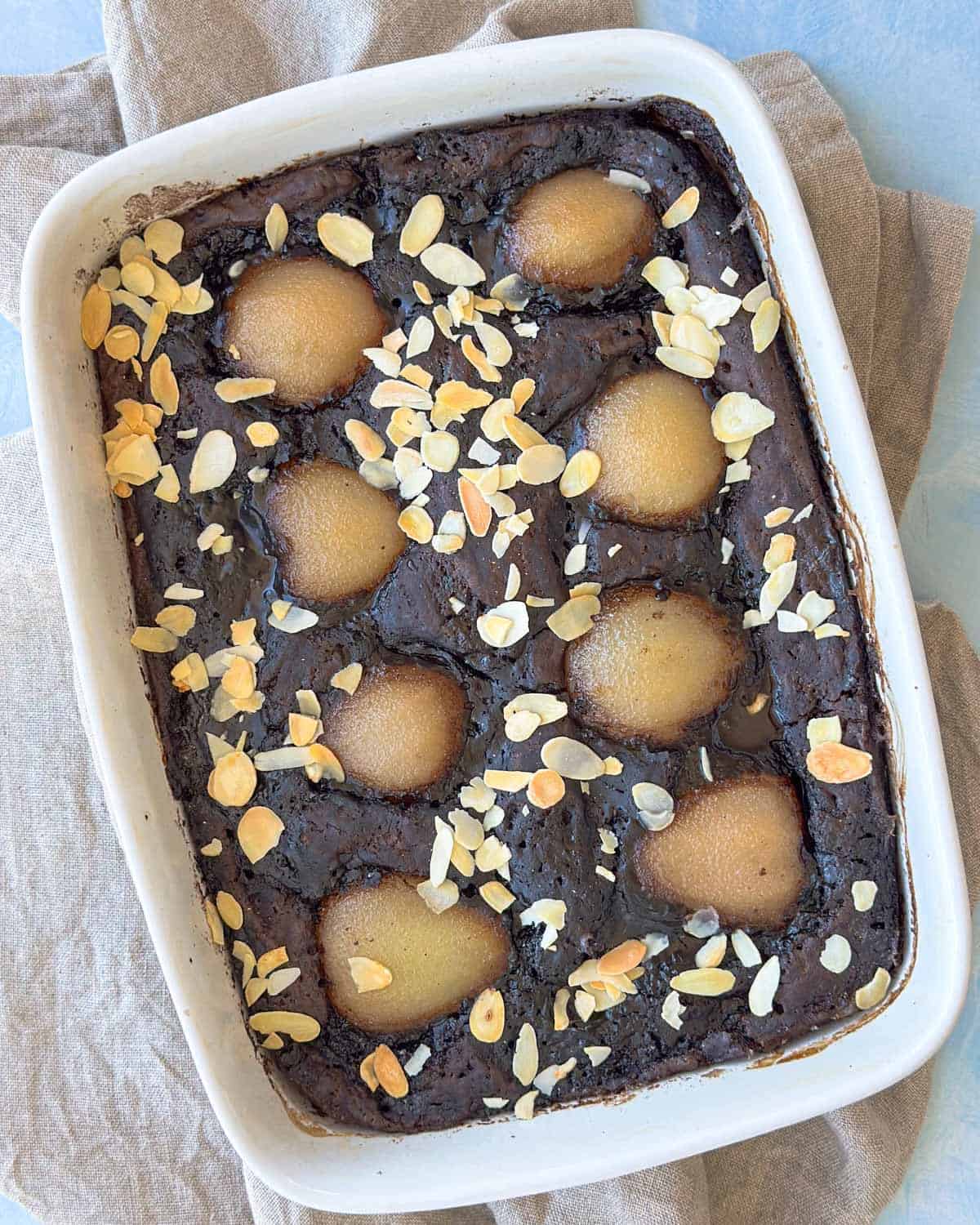 Top-down close-up of a baked chocolate pudding with pears nestled into the batter and finished with sliced almonds for texture.
