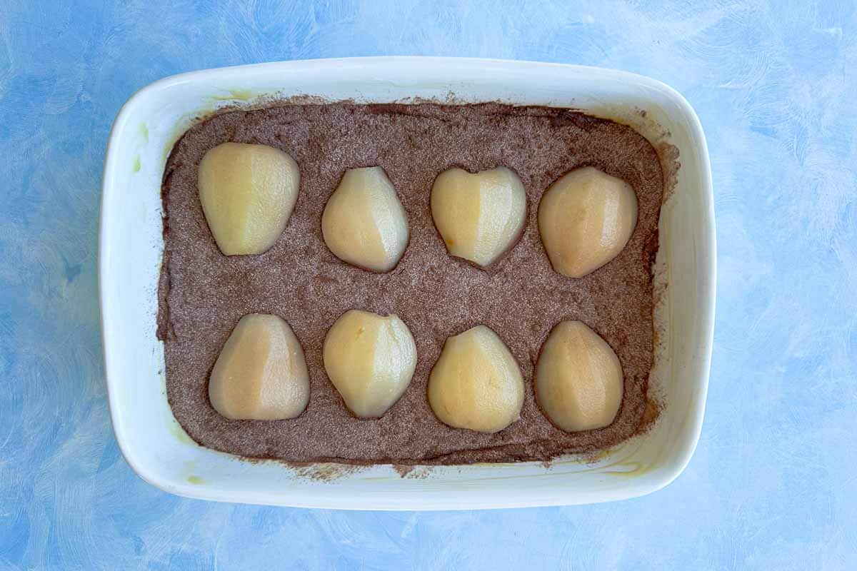 Poached pear halves arranged on top of the cocoa-sugar layer in a single layer before baking.