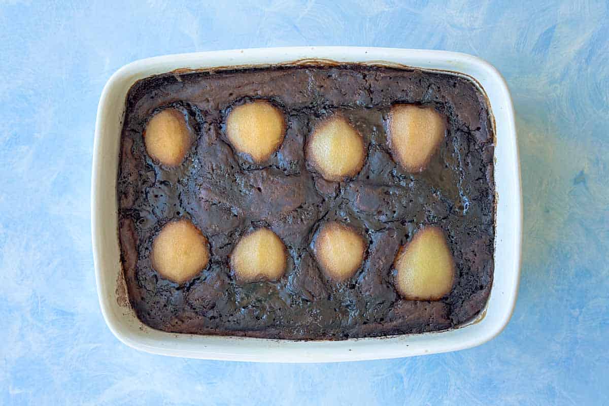 Freshly baked self-saucing chocolate pudding with soft poached pears visible across the surface, straight from the oven.