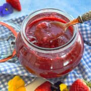 Close-up of homemade strawberry compote in a glass jar with a spoonful lifted to show the thick texture.