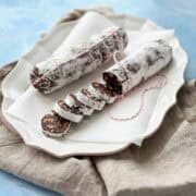 Image of chocolate salami displayed on a serving platter, one log sliced to reveal the rich chocolate interior with cranberries, almonds, and biscuit pieces.