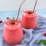 Close-up of two cranberry smoothies showing their thick, creamy texture and garnished with mint and frozen cranberries.