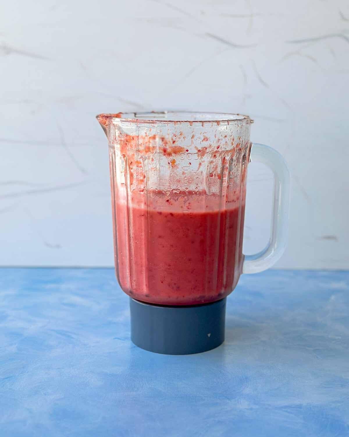 Blended cranberry smoothie mixture in the blender jug, showing the thick, vibrant pink texture after mixing.
