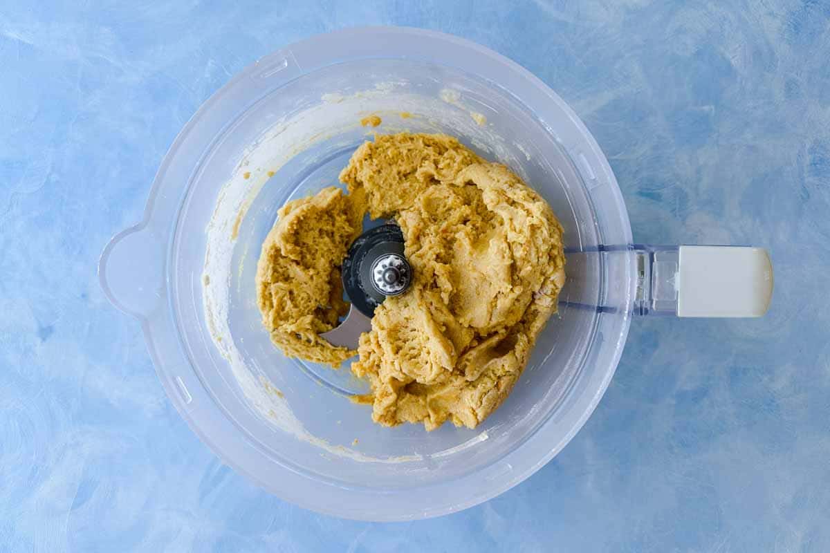 Biscotti dough blended in a food processor, showing a thick, sticky mixture ready for almond folding.