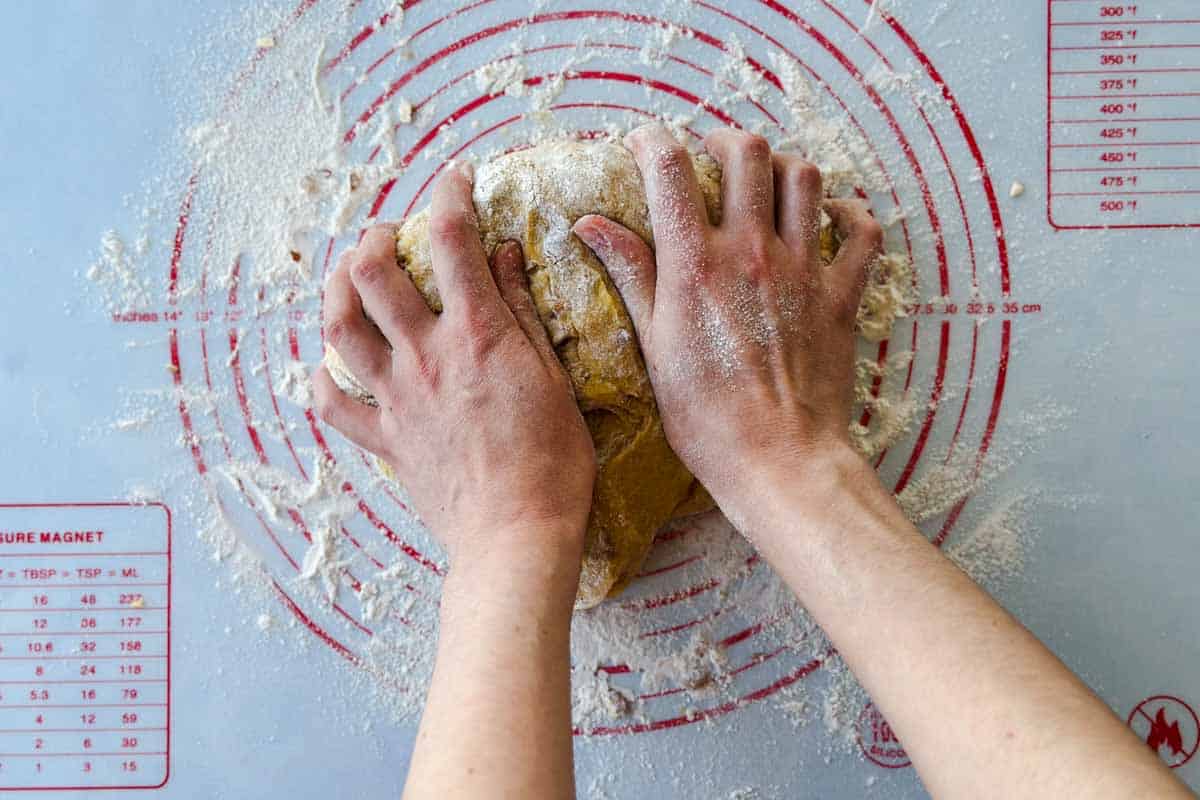 Hands kneading the almond biscotti dough, working it into a smooth, cohesive shape.