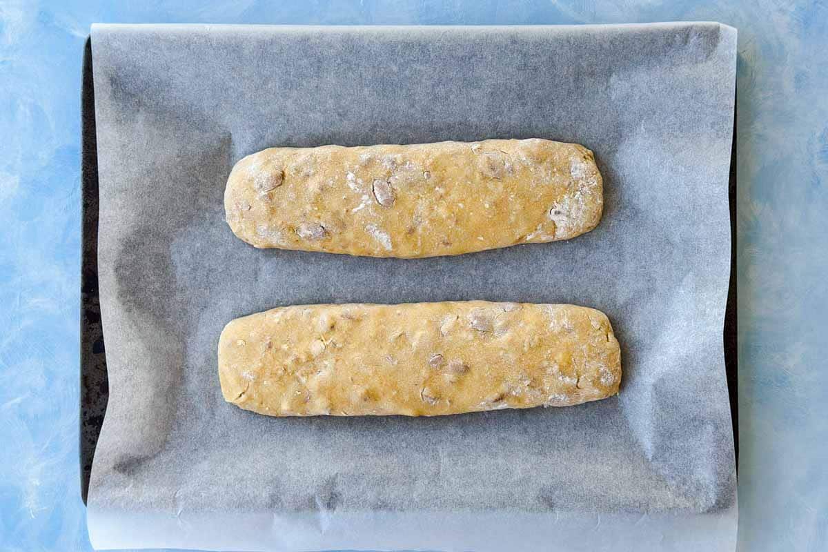 Two shaped biscotti dough logs arranged on a parchment-lined baking sheet, ready for the first bake.