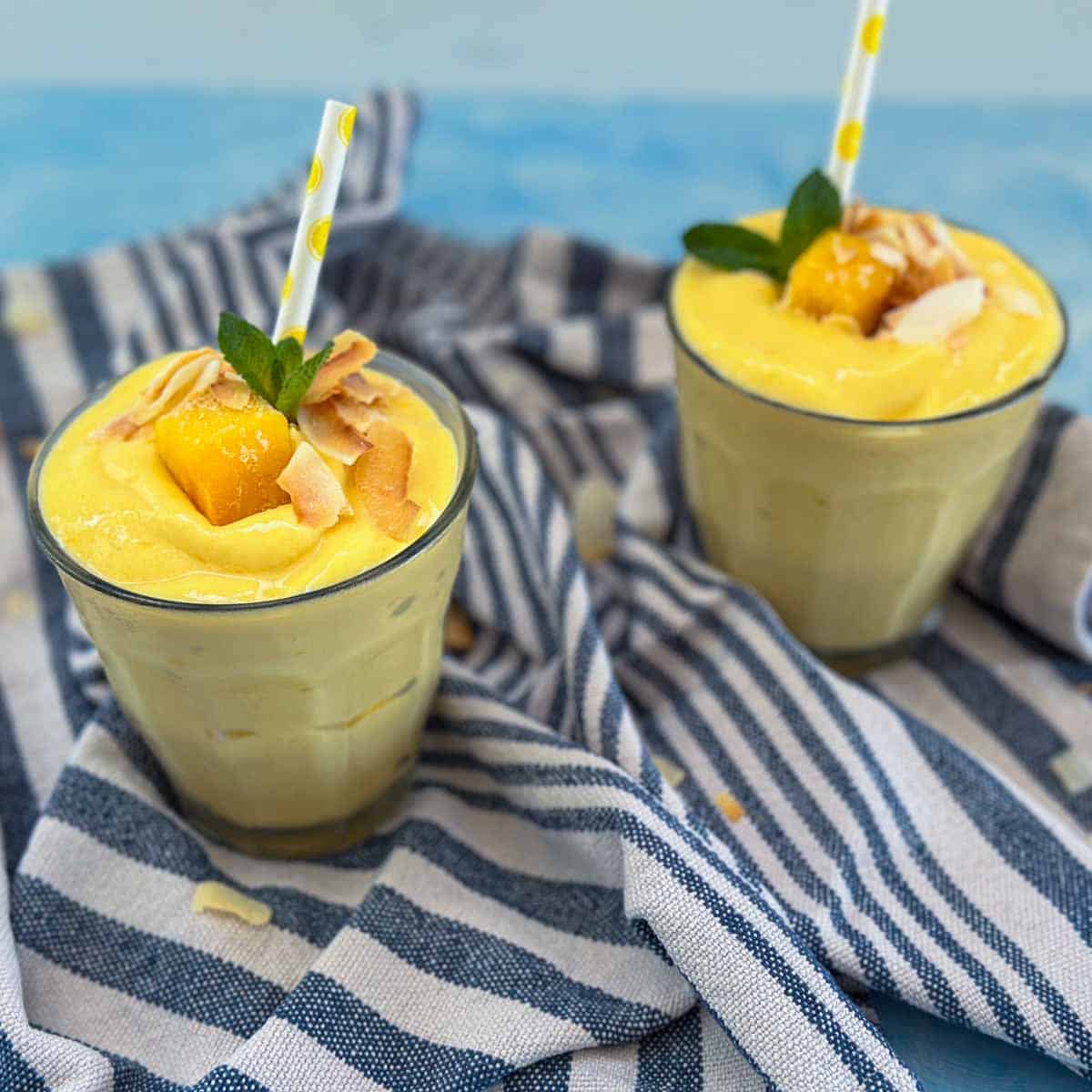 Close up of a thick mango and pineapple smoothie topped with mango chunks, toasted coconut flakes and fresh mint.