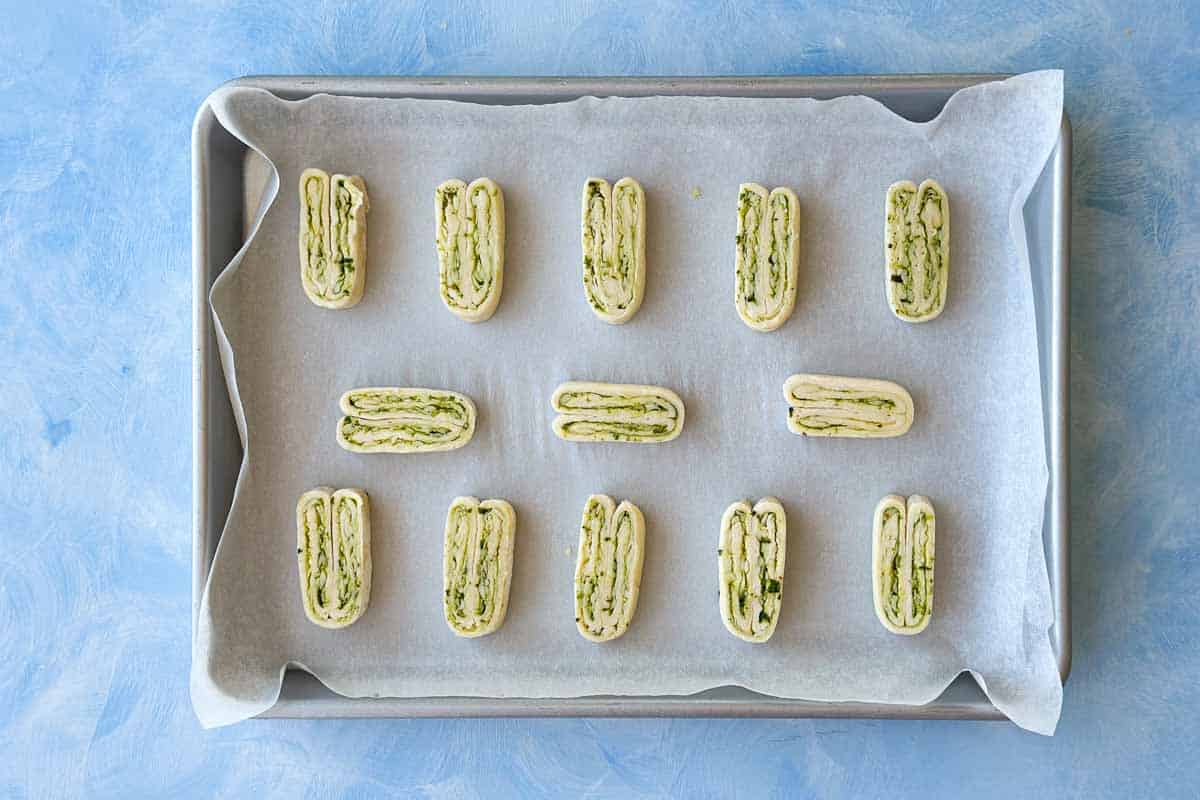 Evenly sliced puff pastry pieces arranged on parchment paper, showing the layered pesto and cheese swirl.