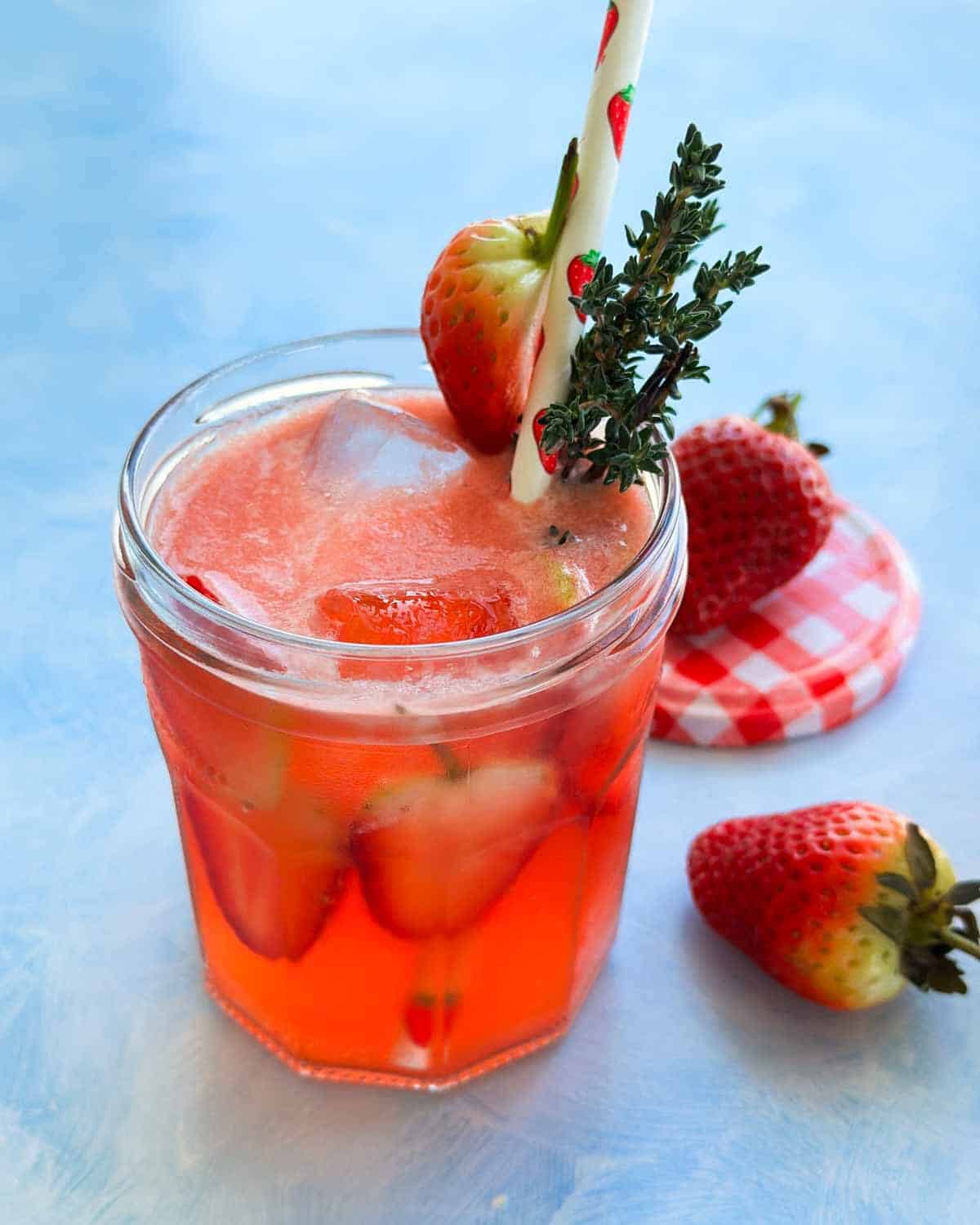 Strawberry gin and tonic cocktail with ice and strawberries, garnished with thyme and a decorative straw.