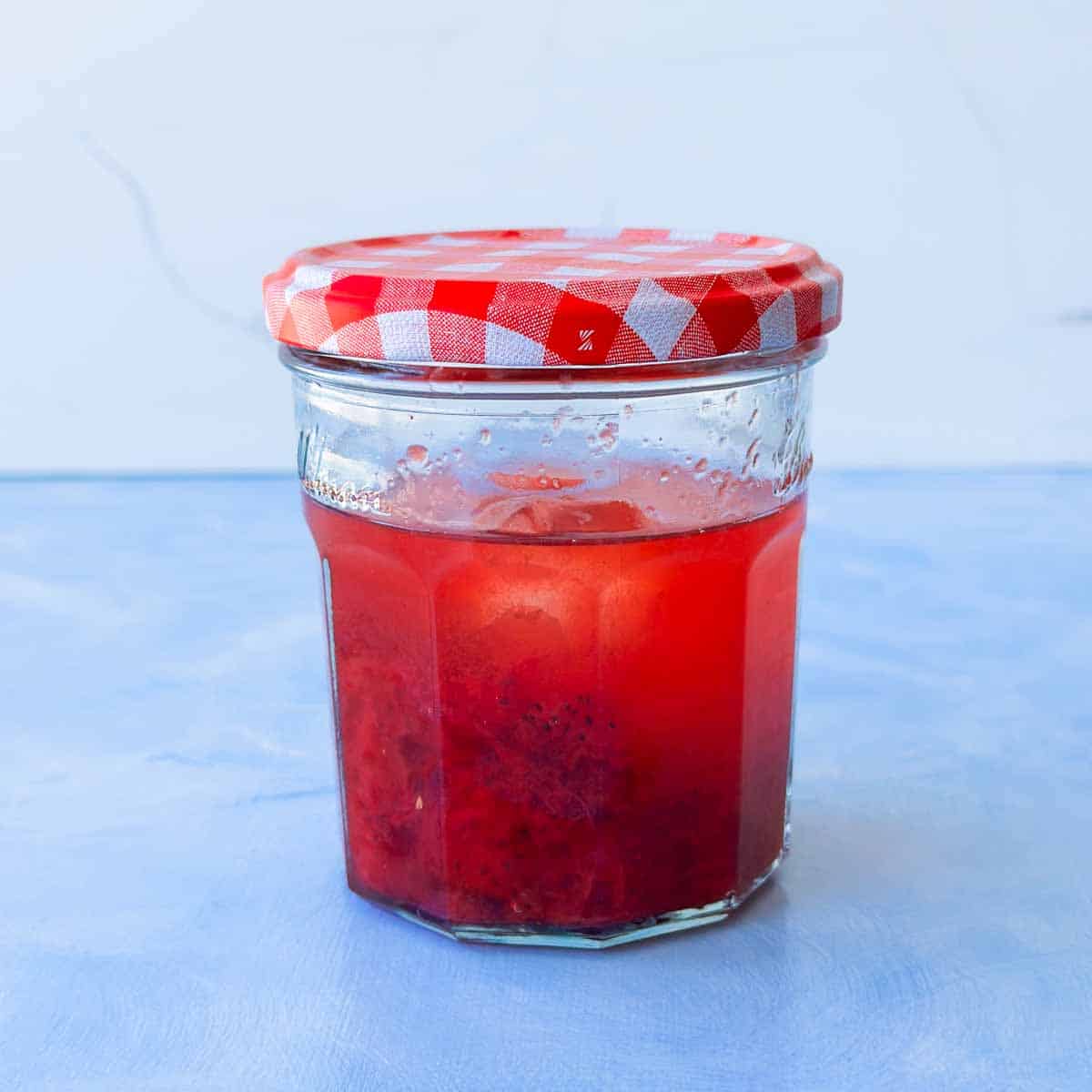 Gin, lemon juice, ice cubes, strawberry jam, and sugar syrup in a sealed jar after being shaken together to mix ingredients.