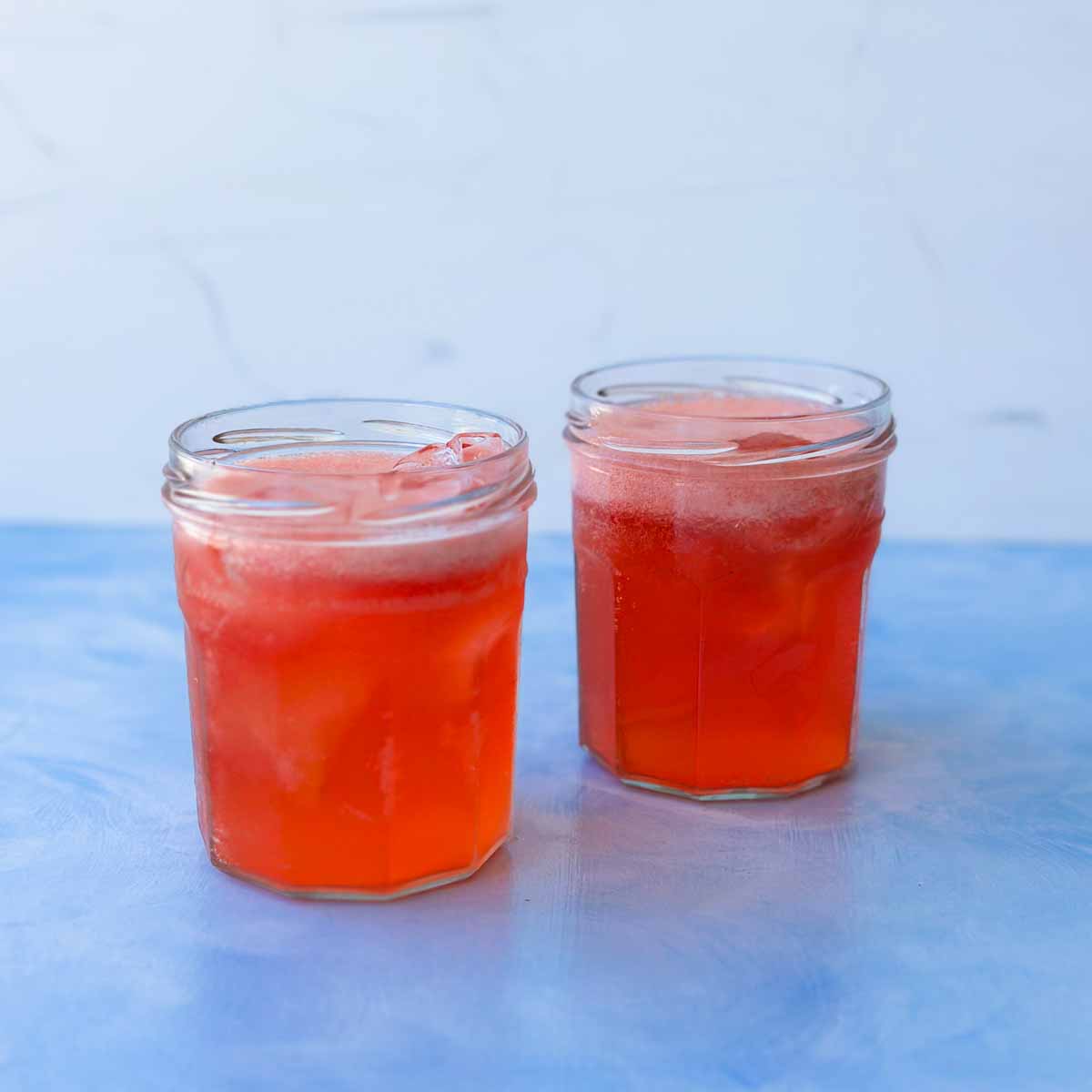 A pair of jars, on a blue counter, with Strawberry gin and tonic mixture, ready to be garnished and enjoyed.