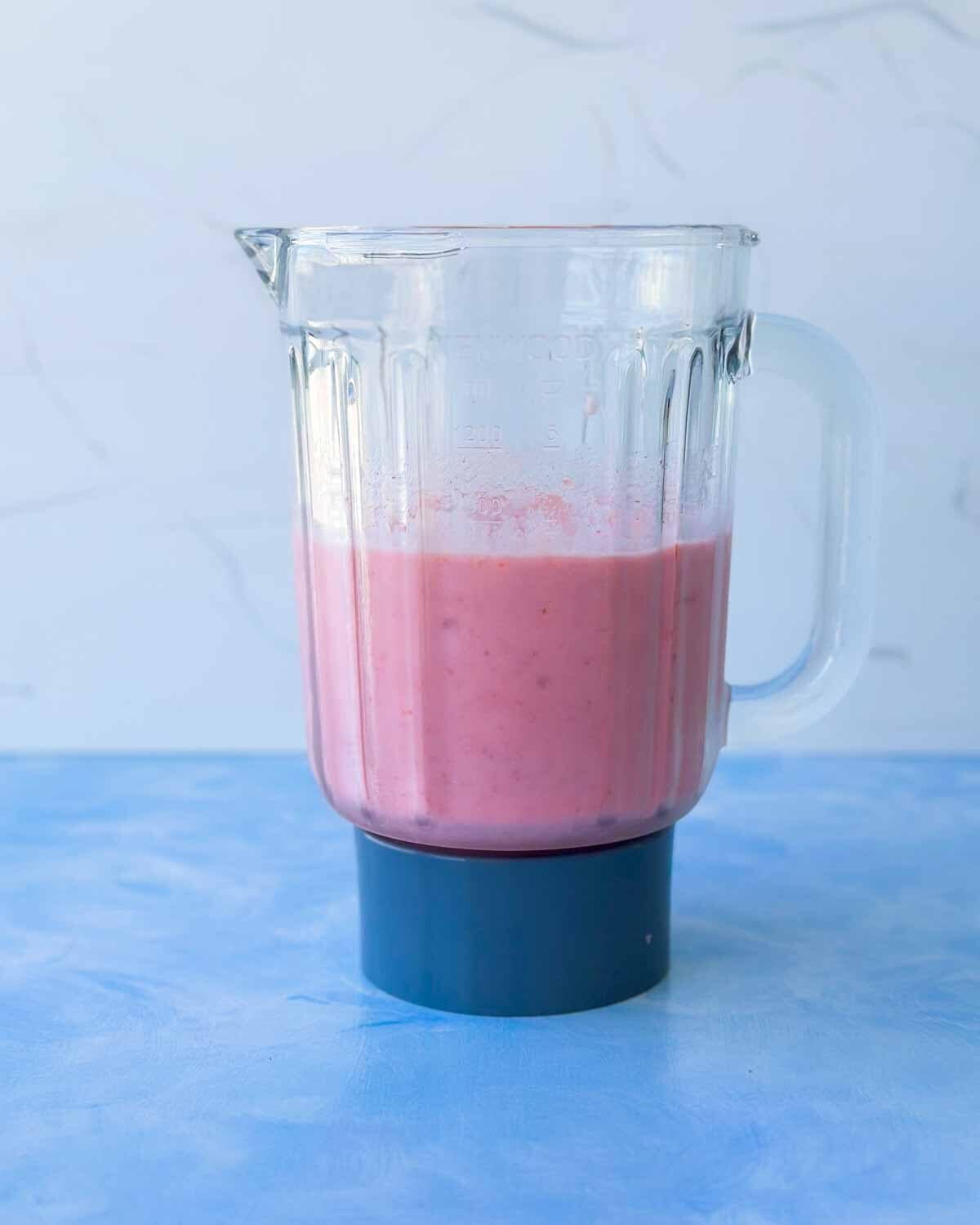 Blended strawberry smoothie mixture in a blender jar, smooth and creamy with a thick pink texture ready to pour into a bowl.