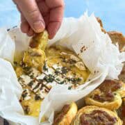Hand dipping a savory palmiers pastry into hot baked camembert, showing the stretchy cheese pull and herbs on top.